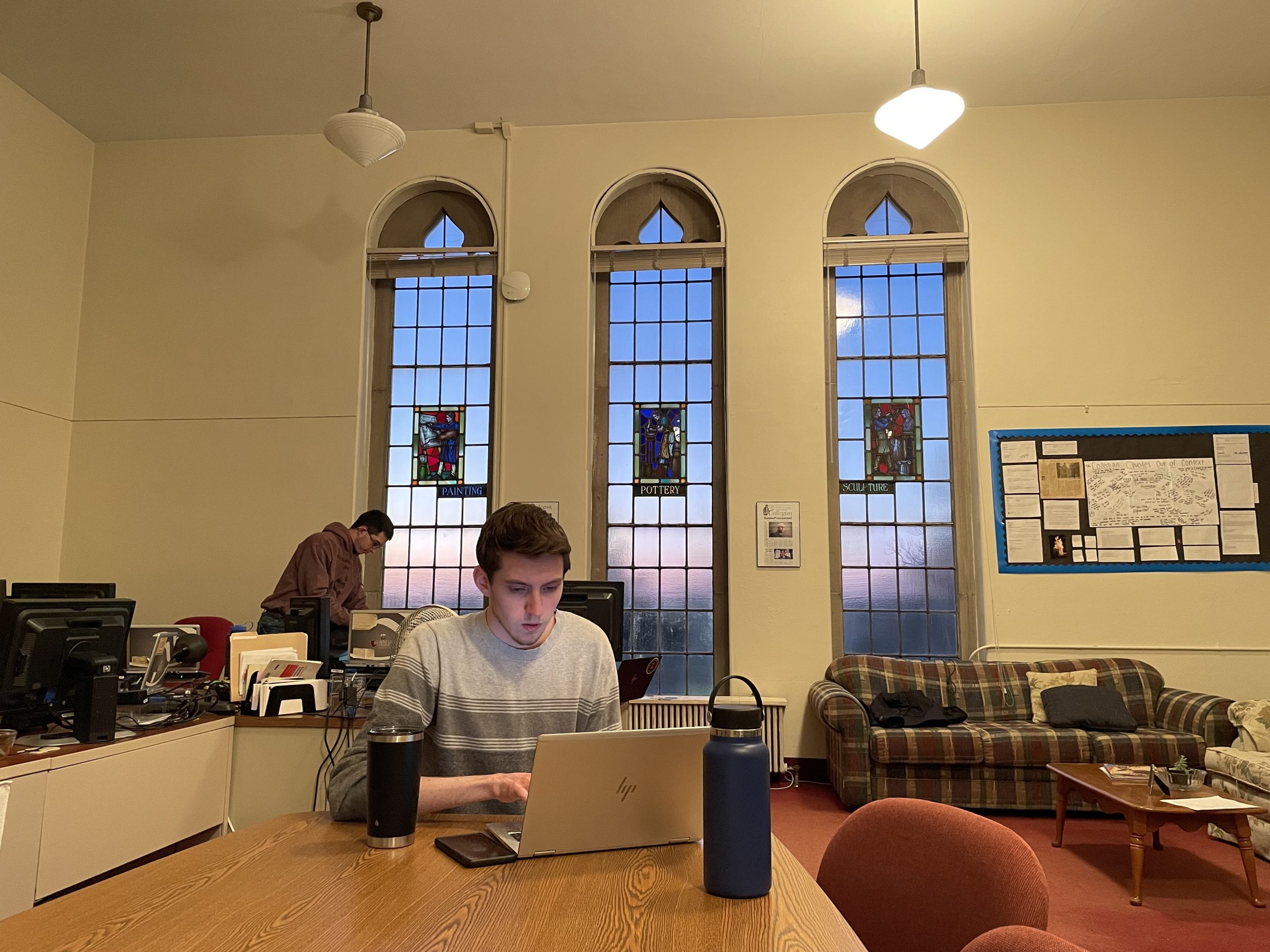 Collegian Editor-in-Chief David Zimmermann works on his weekly “From the Tower” column, completely oblivious to the setting sun’s illumination of the stained glass windows in the newspaper’s office in the tower of Crawford Hall, a gothic structure erected in 1938. The office was originally an art studio and the windows depict painting, pottery and sculpture.